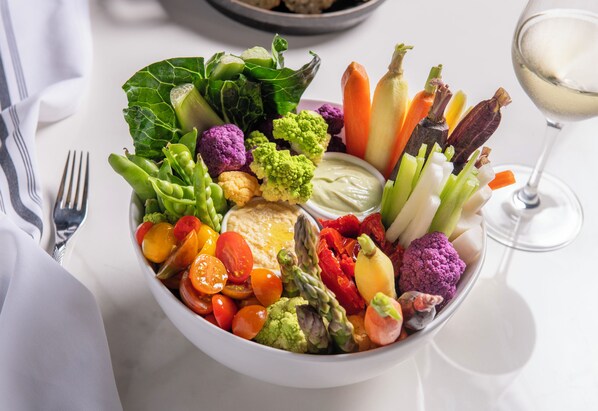 A bowl of assorted vegetables and a glass of white wine on a table.