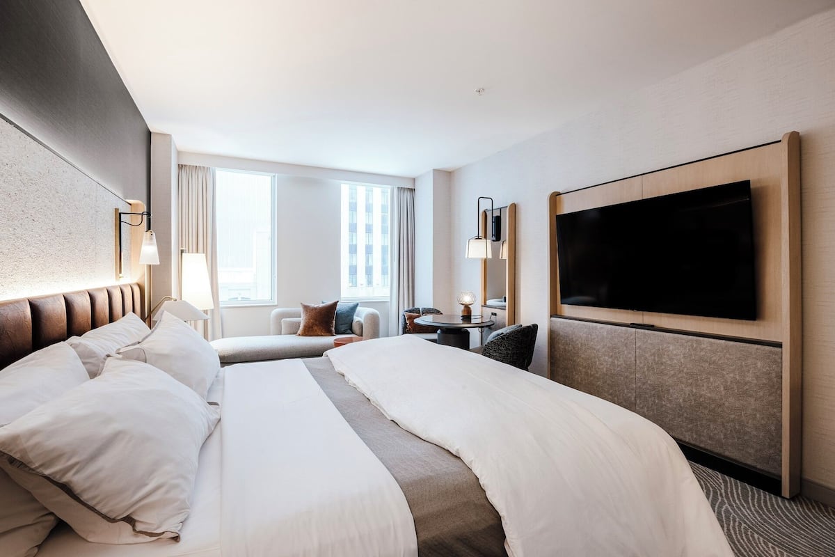 A hotel room with a large bed, a TV, a desk, and a window with curtains.