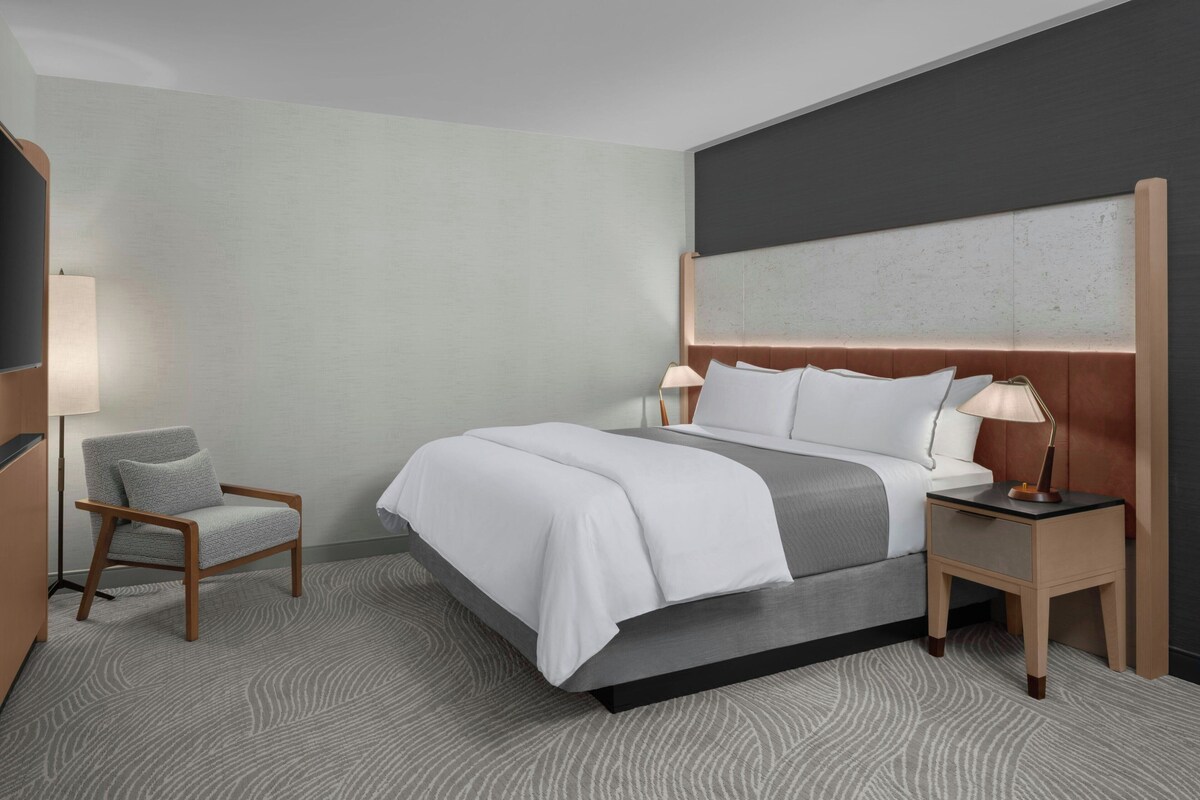 Ein Hotelzimmer mit einem Bett, einem Sessel, einem Nachttisch und einer Lampe.