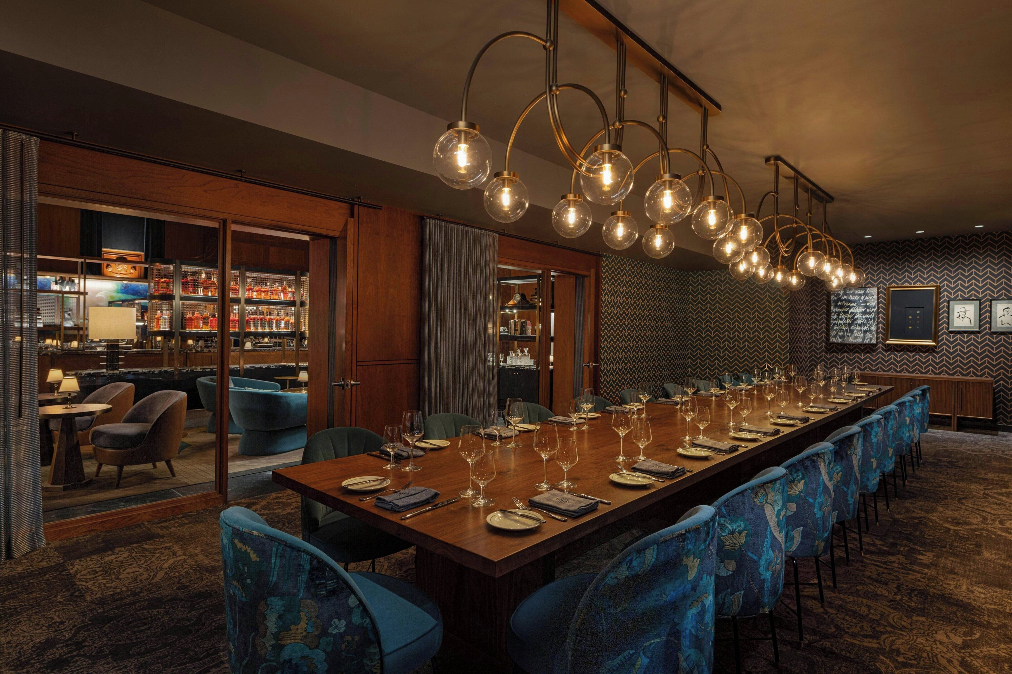 A long dining table set with chairs, a bar area with shelves of bottles, and a patterned wall.