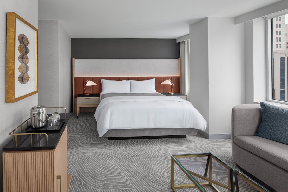 A hotel room with a large bed, bedside lamps, a sofa, a coffee table, and a view of the city.