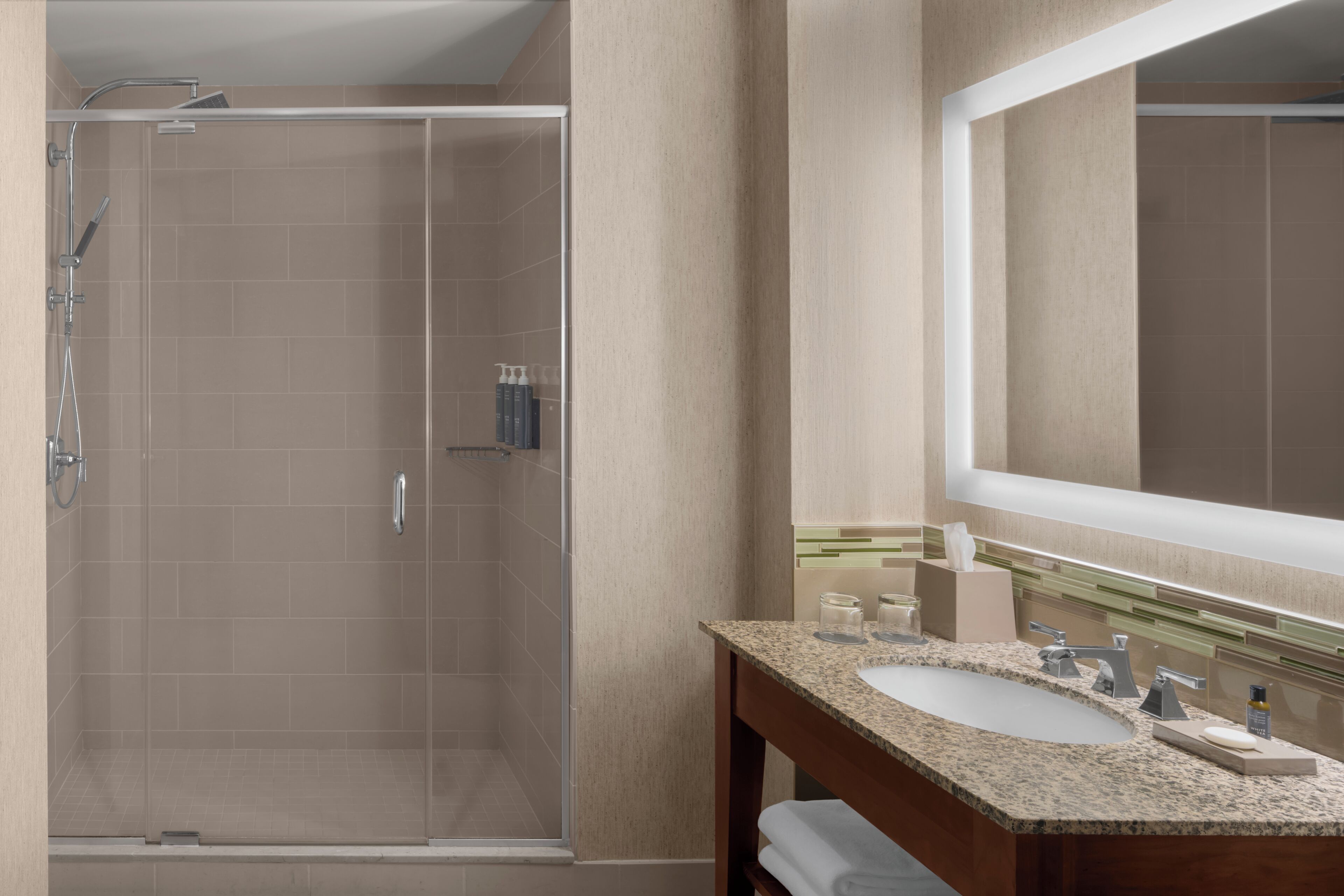 Un baño moderno con ducha de vidrio, lavabo con tocador y un espejo grande.