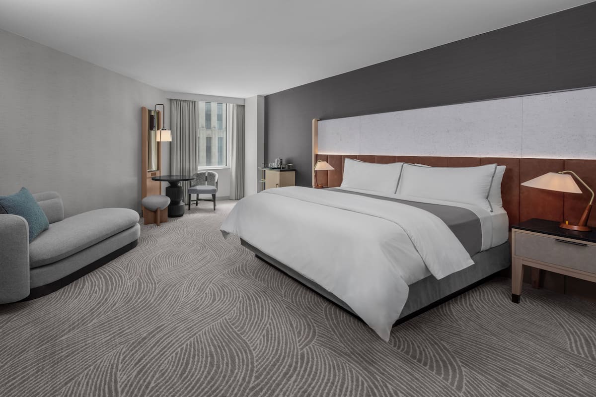 A modern hotel room with a large bed, a desk, a chair, and a view of the city.