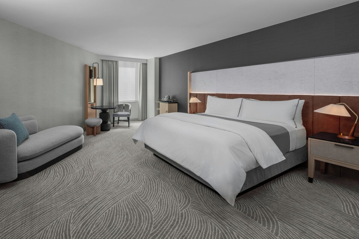 Ein modernes Hotelzimmer mit einem großen Bett, einem Schreibtisch, einem Stuhl und Blick auf die Stadt.
