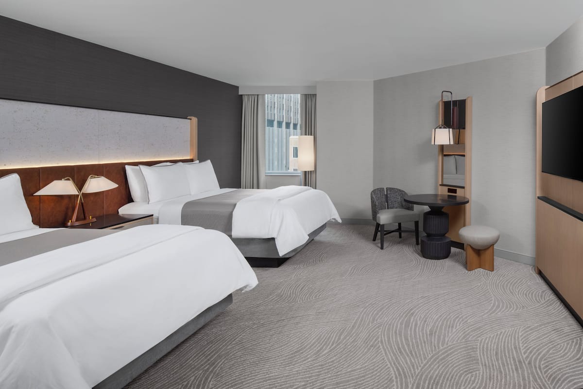 A hotel room with two beds, a desk, a chair, a TV, and a window with curtains.