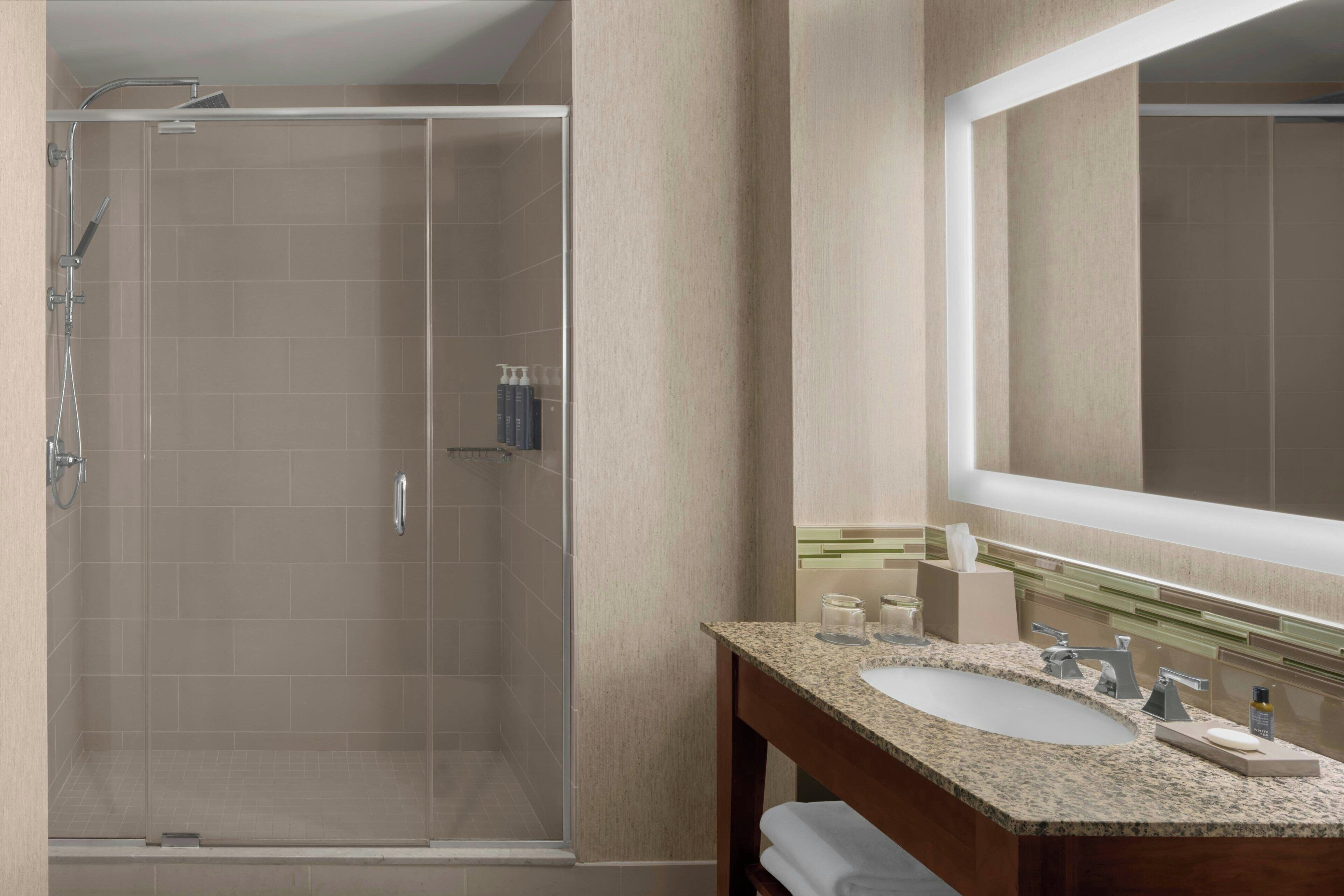 A modern bathroom with a glass-enclosed shower, a large mirror, and a granite countertop sink.