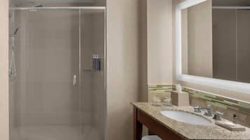 A modern bathroom with a glass-enclosed shower, a large mirror, and a granite countertop sink.