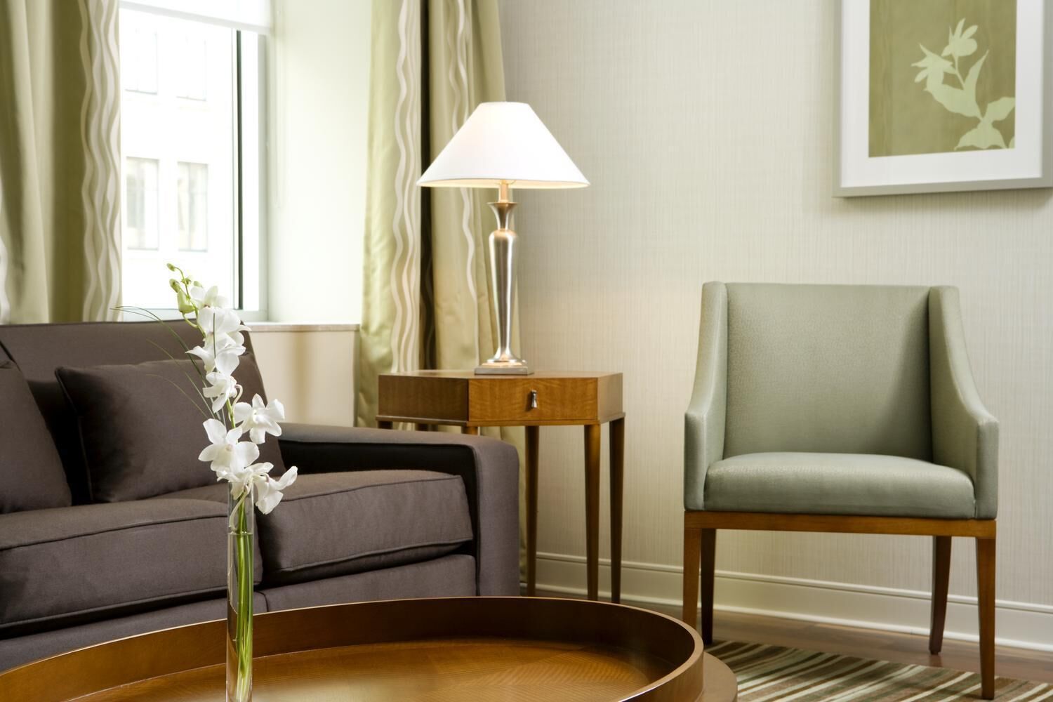 A living room with a sofa, a chair, a lamp, a side table, and a vase with flowers.