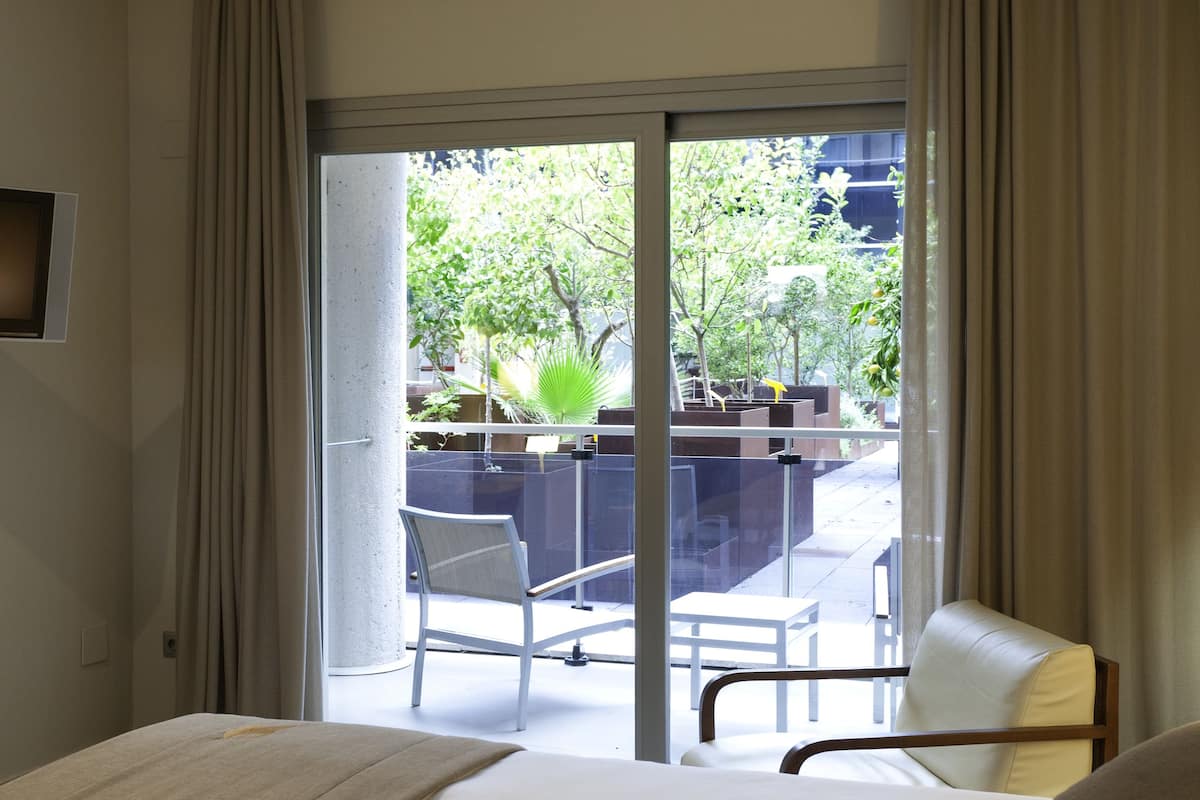 A hotel room with a large bed, a chair, and a view of an outdoor area with a table and chairs.