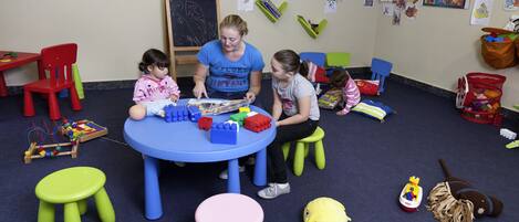 Una habitación con una mesa azul, taburetes verdes y juguetes infantiles.