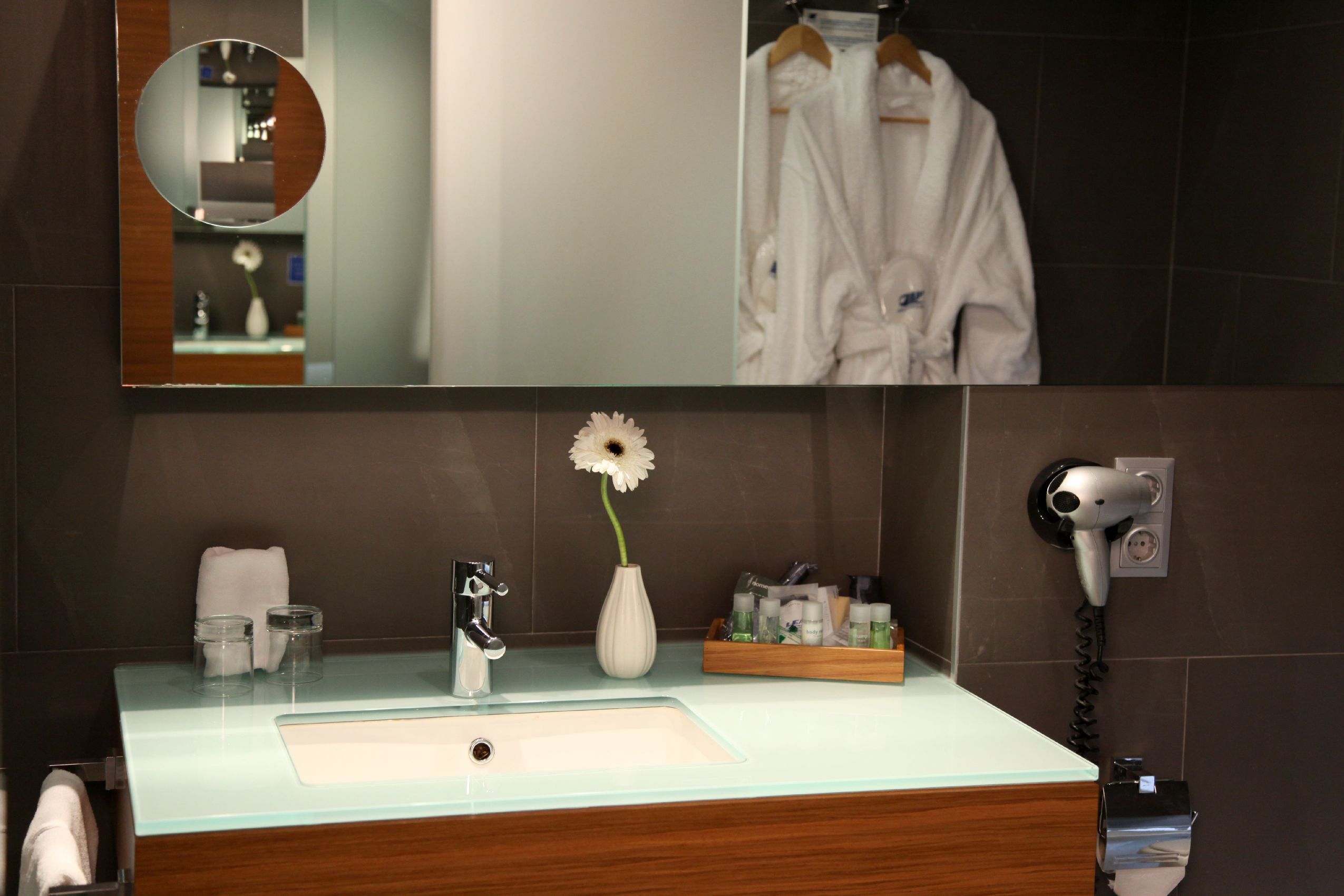 Une salle de bain équipée d’un lavabo en verre, d’un miroir, d’un sèche-cheveux et d’articles de toilette.