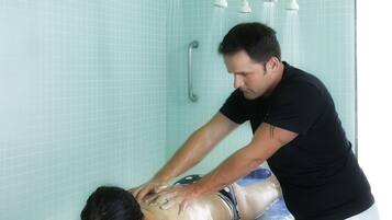 Una persona recibiendo un masaje en la espalda en una bañera con múltiples cabezales de ducha.