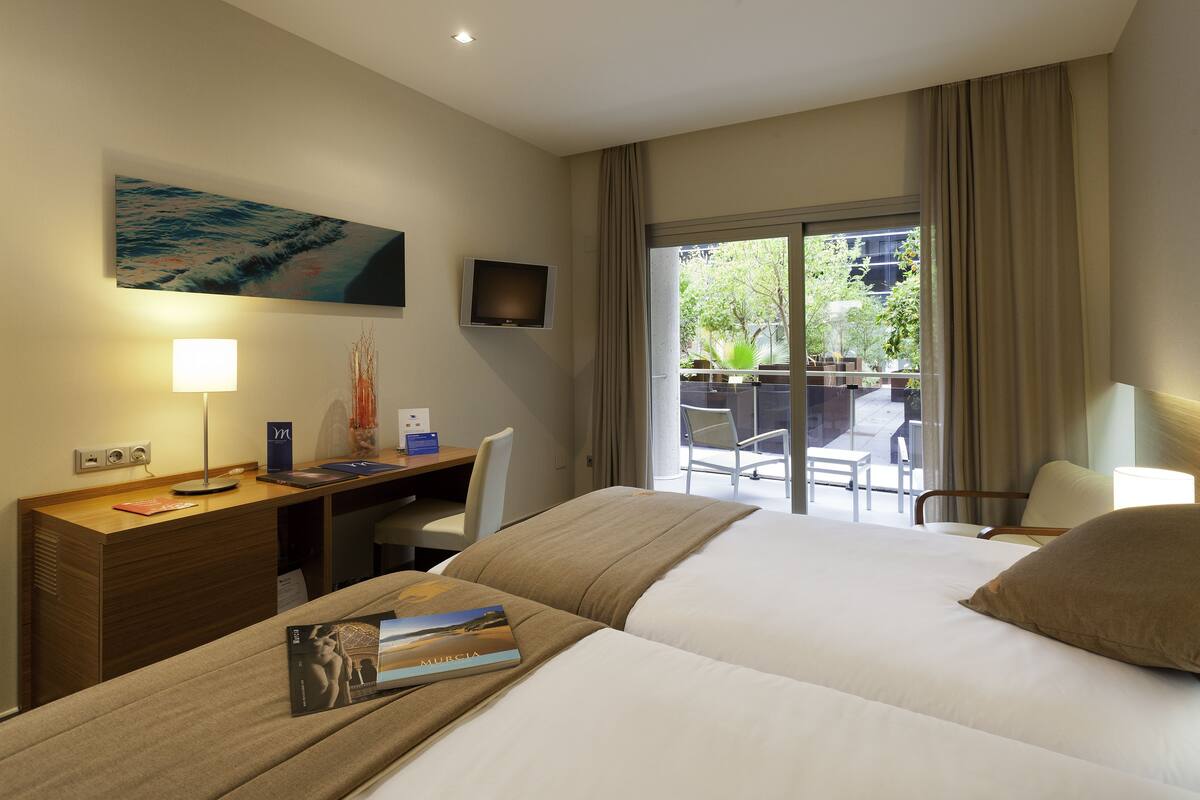 A hotel room with a bed, a desk with a computer, a chair, a TV, and a view of the outdoors.