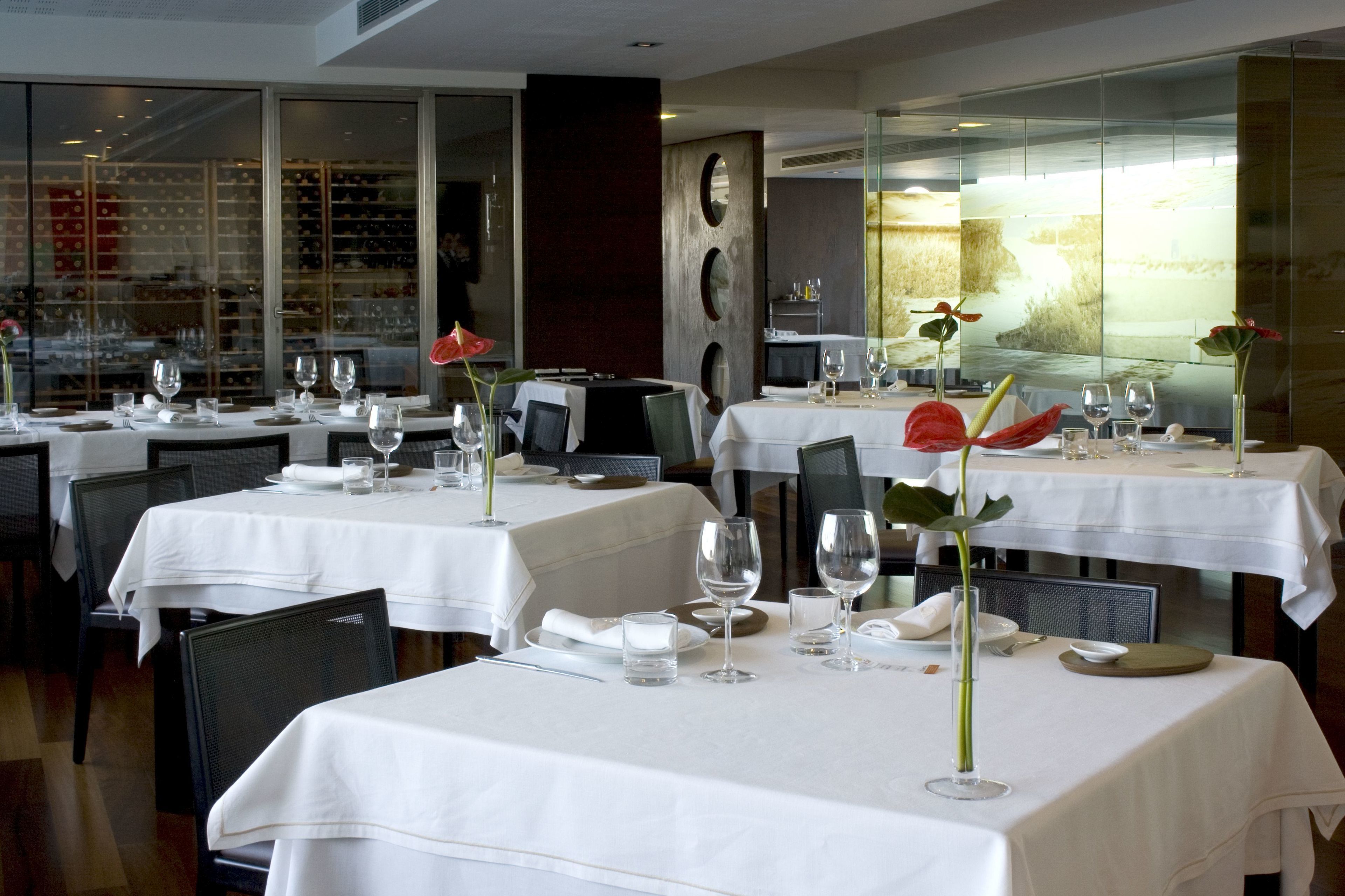 Un restaurante con varias mesas dispuestas para comer, cada una con manteles blancos y copas de vino.