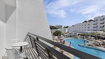 Balcón con vista a la piscina, muebles blancos y cielo despejado.