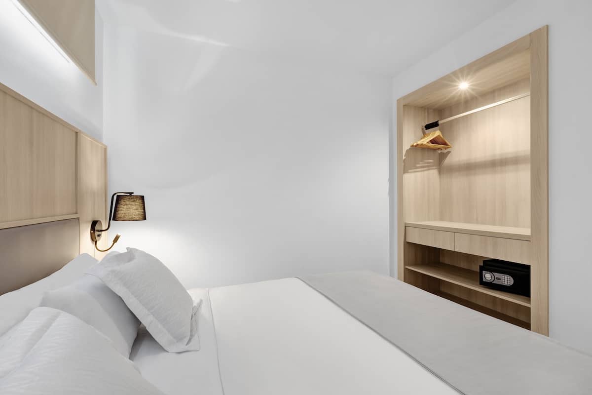 Una habitación de hotel moderna con una cama bien hecha, un estante en la pared con una radio y una lámpara de noche.