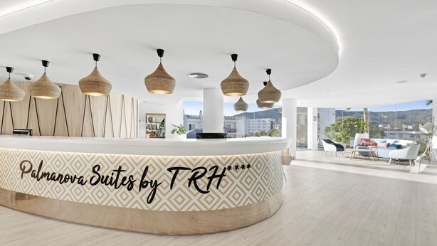 A modern reception area with a curved counter, hanging pendant lights, and a view of the cityscape. - Palmanova Suites by TRH (Calvia)