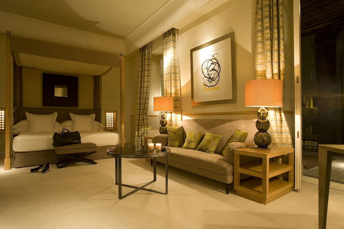 A hotel room with a bed, a sofa, a coffee table, and a lamp.