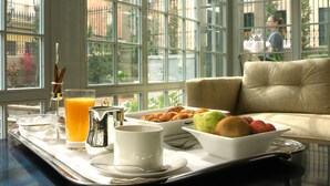 A breakfast tray with croissants, fruit, a coffee cup, and orange juice on a table by a window with a view of buildings and greenery. - Villa Oniria (Granada)