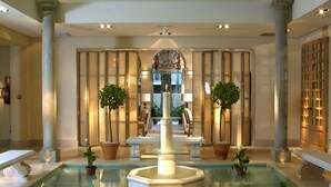 A spacious lobby with a central fountain, marble columns, and potted plants. - Villa Oniria (Granada)