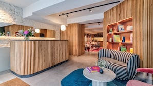 A modern reception area with a wooden reception desk, a seating area with striped sofas, and a bookshelf with books and decorative items. - Republik Hôtel (Lyon)