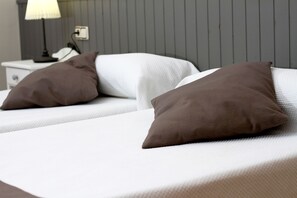 Una cama con dos almohadas, una mesita de noche con una lámpara y una pared con líneas verticales.