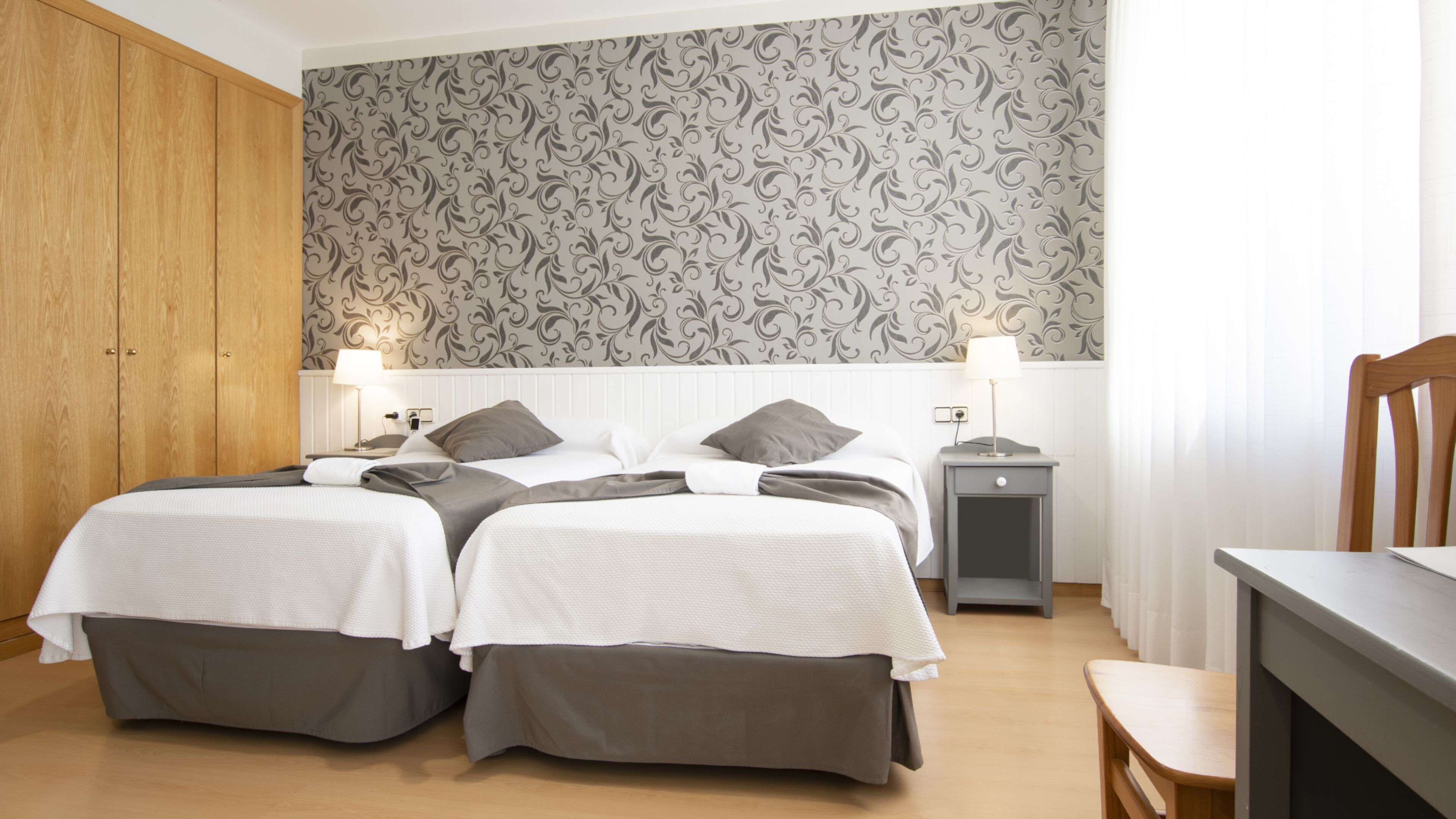 A double room with two beds, a wooden wardrobe, a nightstand, and a desk with a chair.