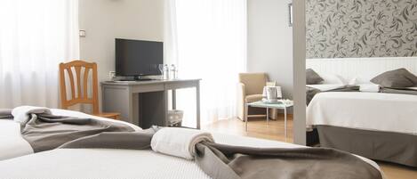 A hotel room with two beds, a desk with a TV, a chair, and a small table with a bottle and glass.