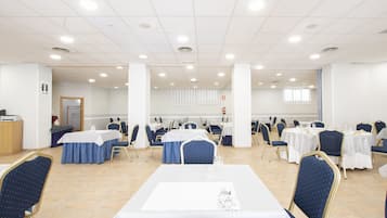 Un salón de conferencias con varias mesas y sillas, paredes blancas y luces en el techo.