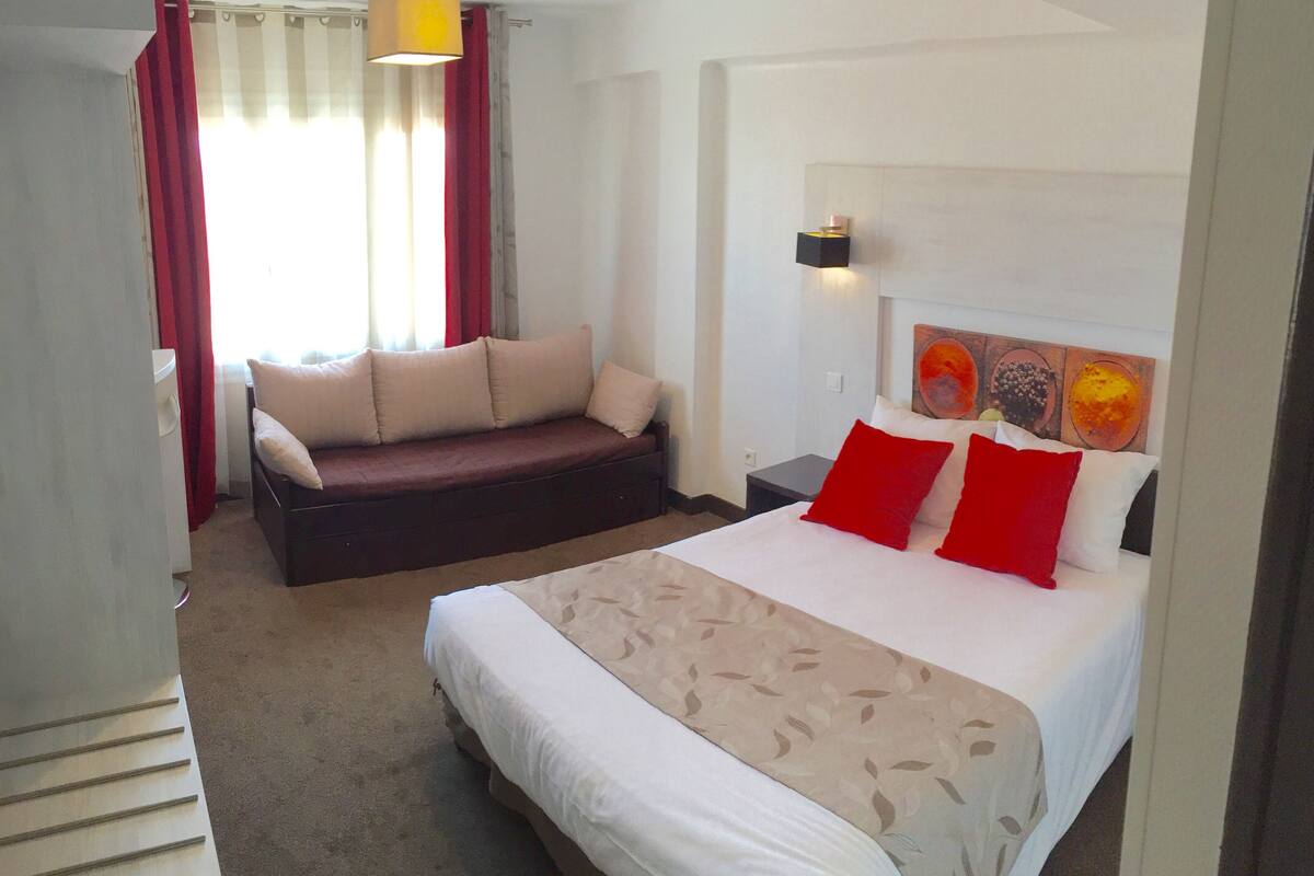 A hotel room with a bed, a sofa, a nightstand, and a wall with artwork.