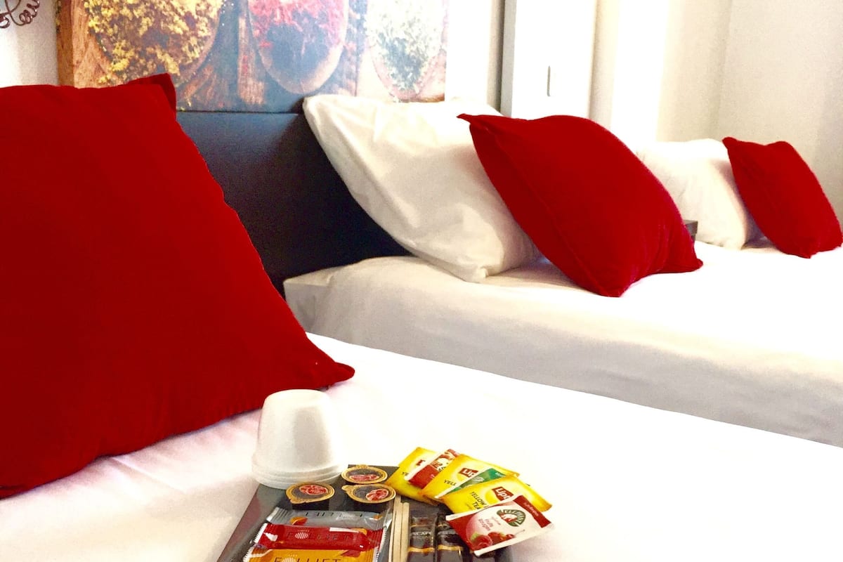 A hotel room with two beds, each with white bedding and red pillows. A tray with snacks and a bottle is placed on the bed.