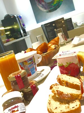 Una mesa de desayuno con croissants, un tarro de Nutella, un vaso de jugo de naranja y una taza de café.