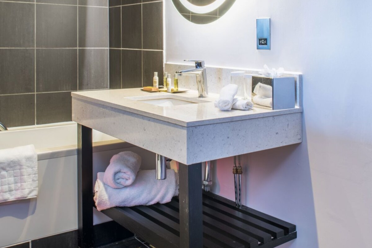 A modern bathroom with a large mirror, a sink, and a bathtub.