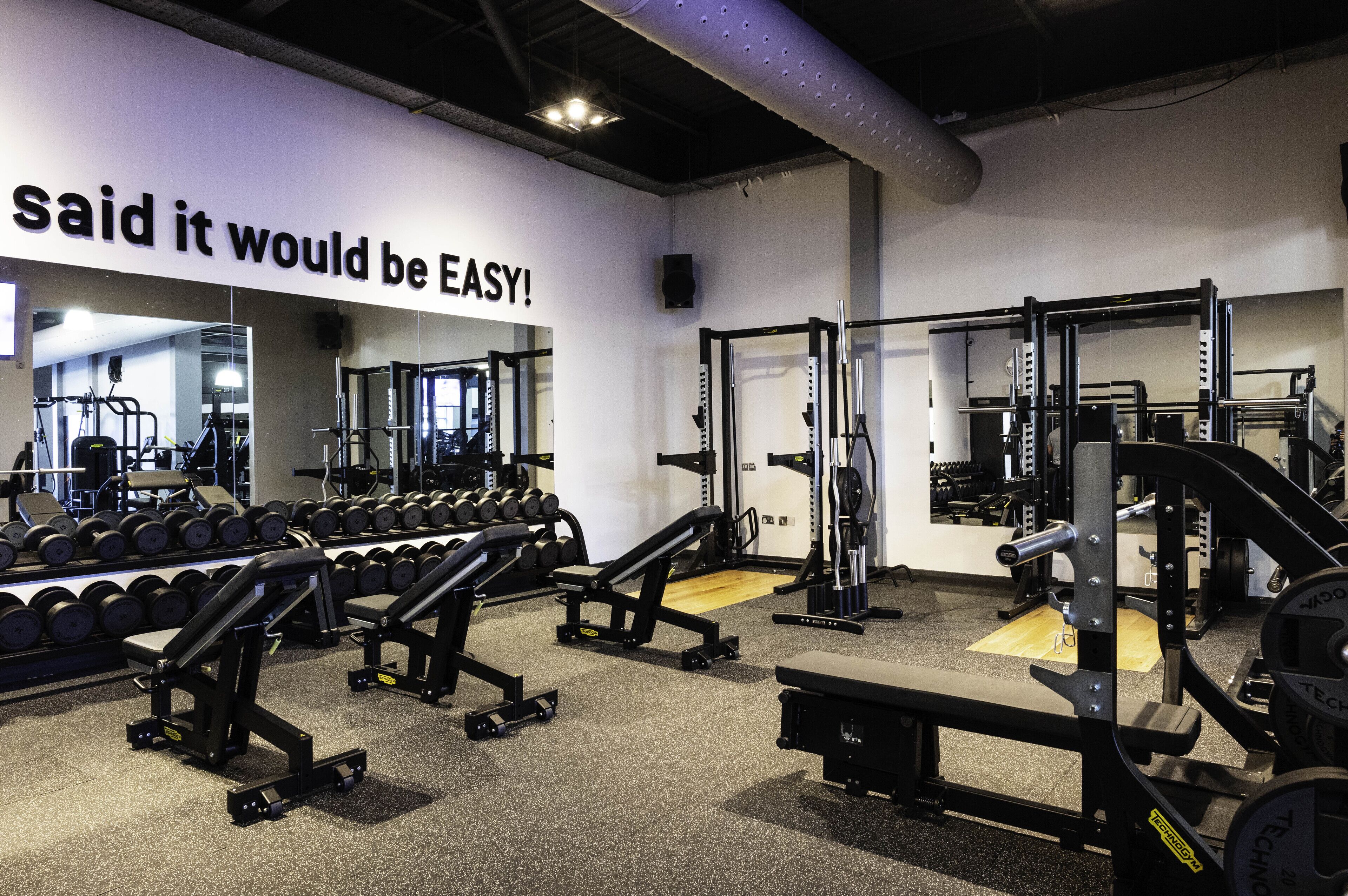 A gym with weightlifting equipment, mirrors, and a motivational quote on the wall.