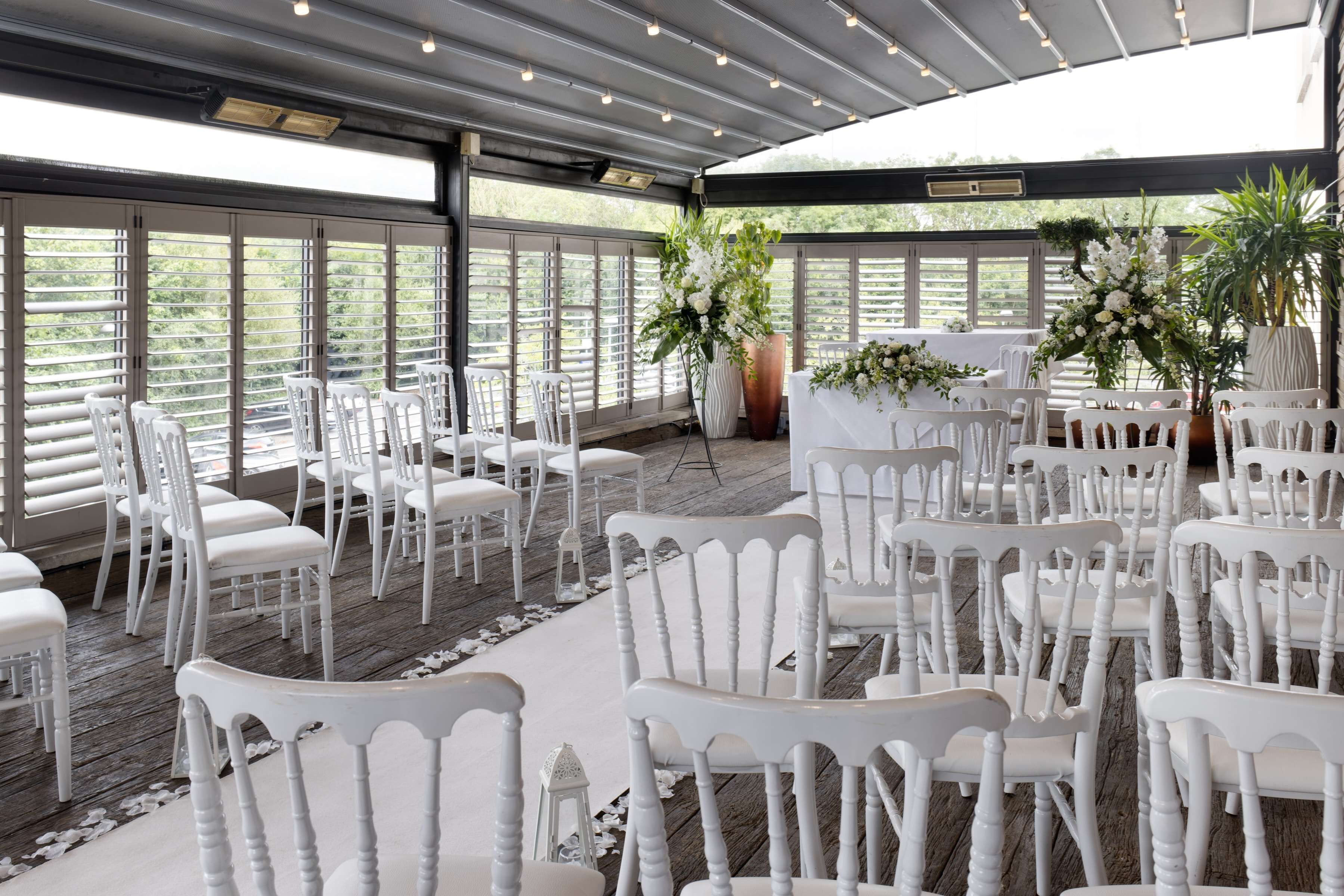 An indoor venue with white chairs arranged in rows, large windows, and potted plants.