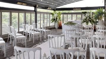 An indoor venue with white chairs arranged in rows, large windows, and potted plants.