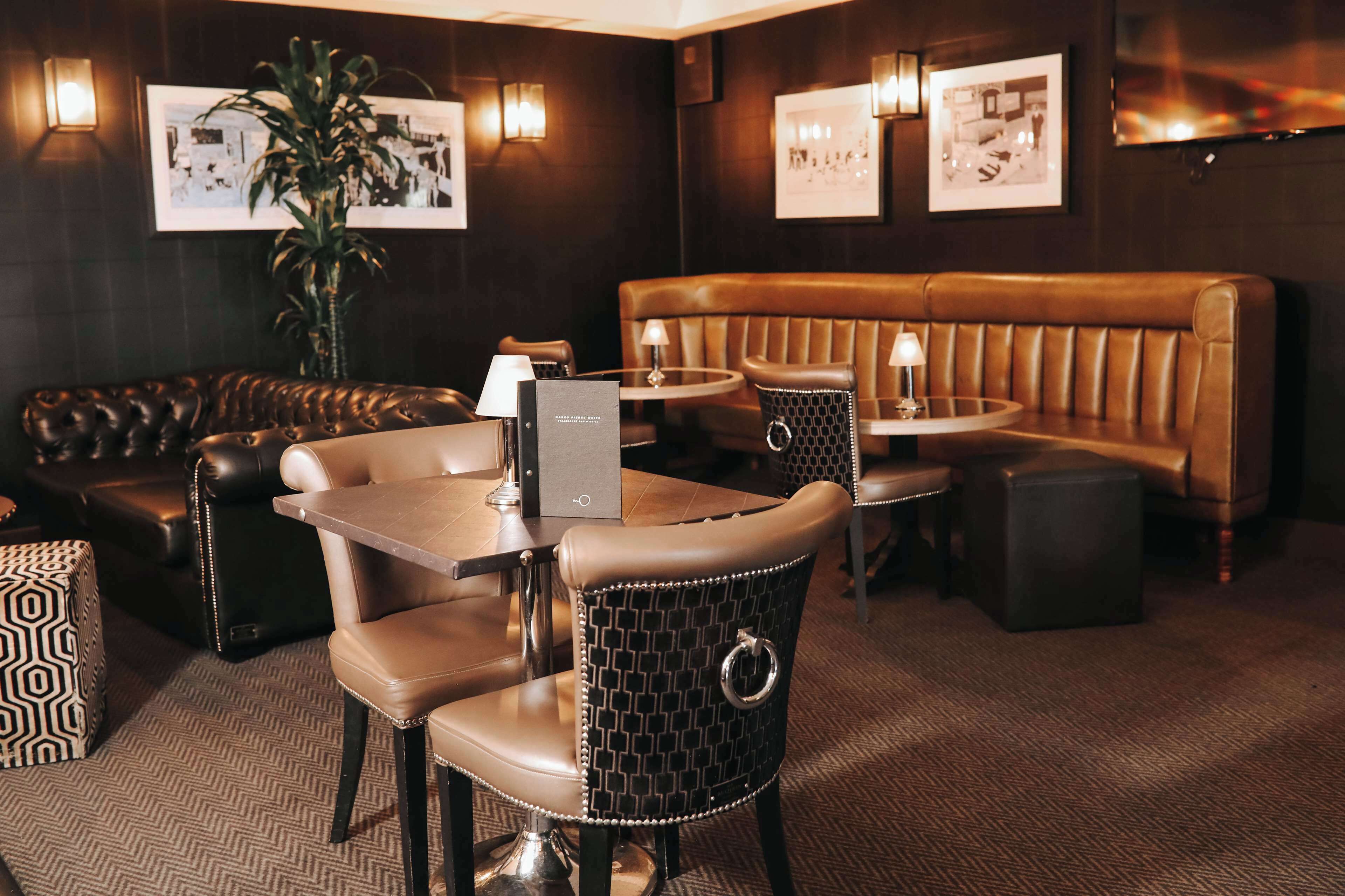 A cozy restaurant interior with leather seating, tables, and framed pictures on the walls.