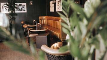 A cozy indoor seating area with a leather sofa, a round table, and a small round table. There are framed pictures on the wall and a potted plant in the foreground.
