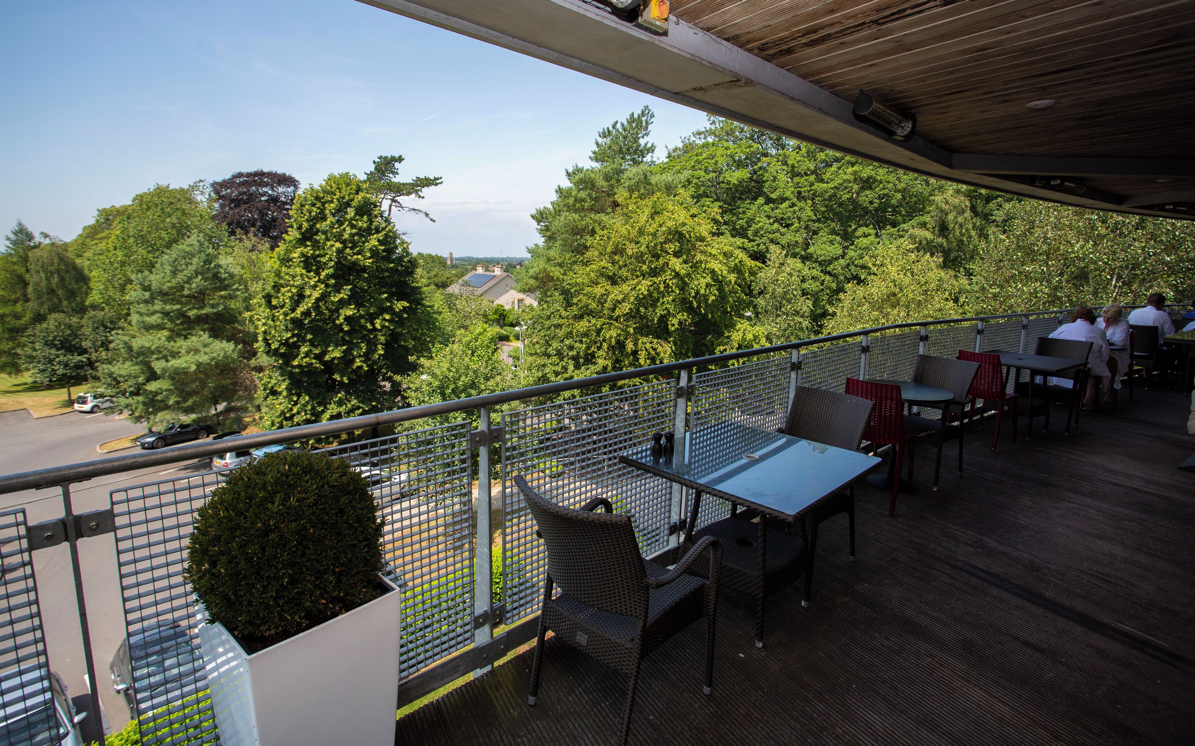 A balcony with outdoor seating, a view of trees and houses, and a metal railing.