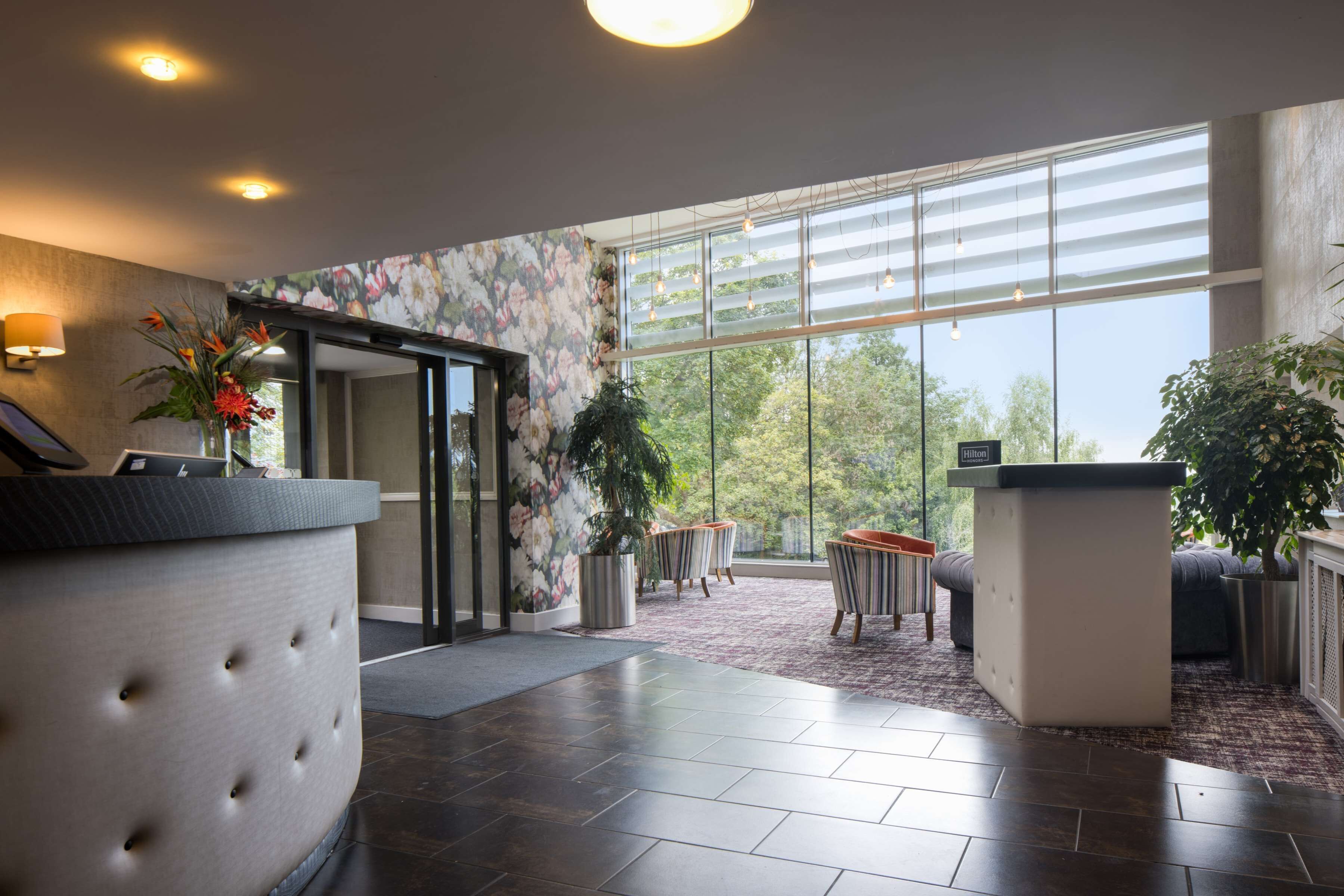 A modern hotel lobby with a reception desk, seating area, and large windows offering a view of the outdoors.