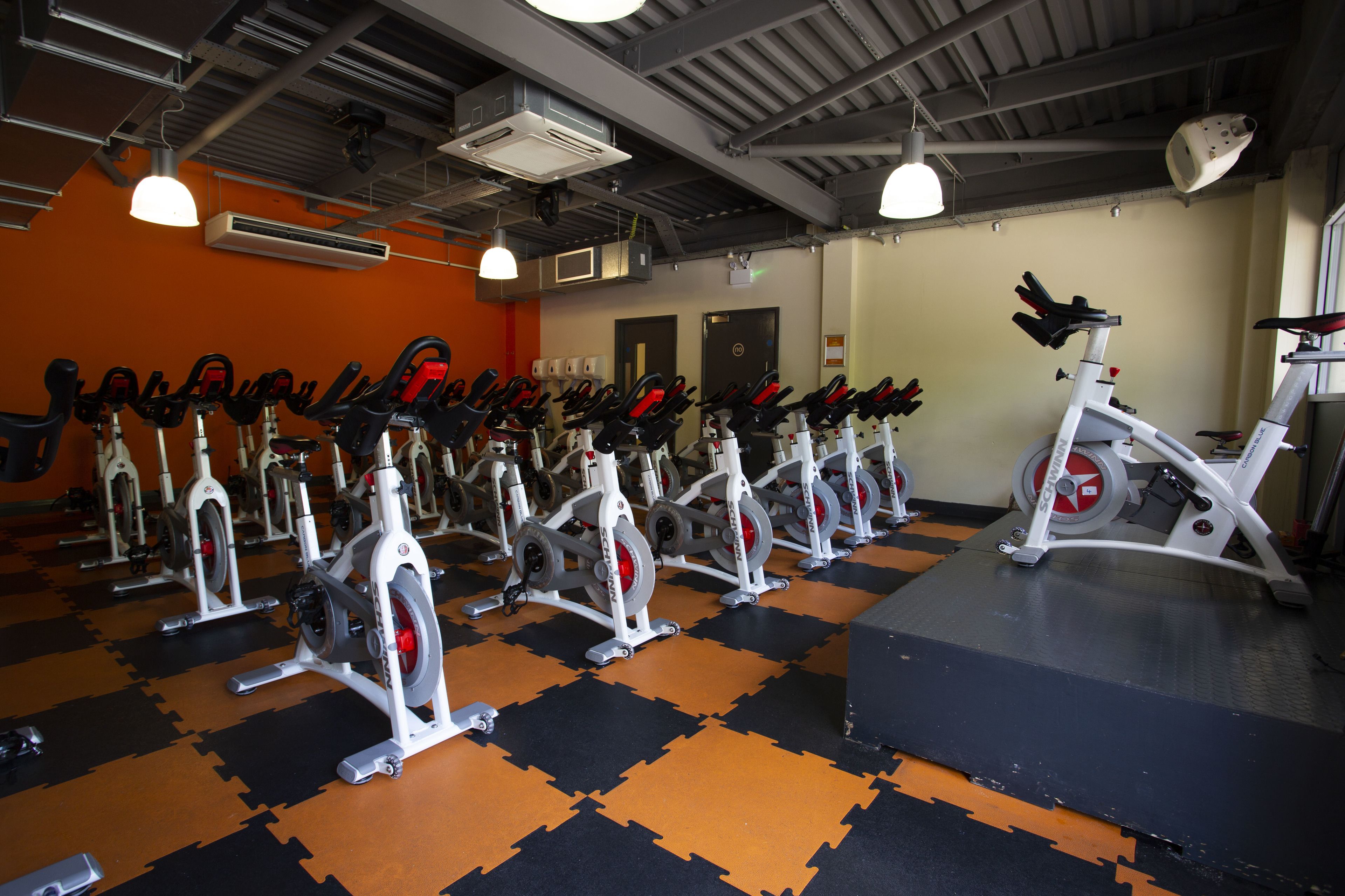A gym with stationary bikes arranged in rows, a large mirror, and a black and orange floor.