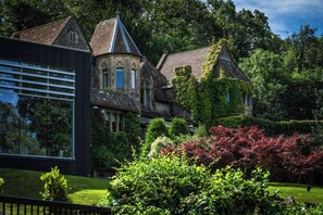 Edificio histórico con amplia fachada de vidrio y arquitectura tradicional, rodeado de exuberante vegetación y plantas en flor.