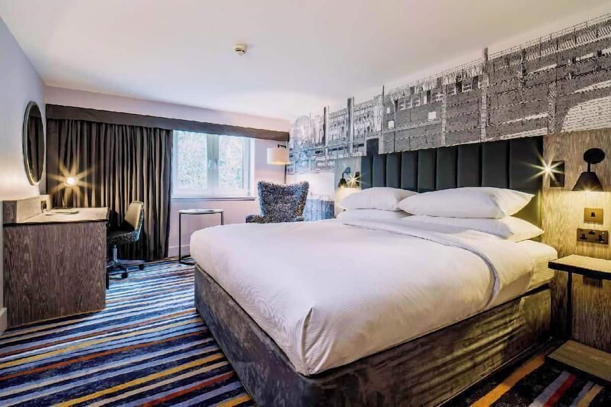 A hotel room with a large bed, a desk, a chair, a window with curtains, and a wall with a textured design.