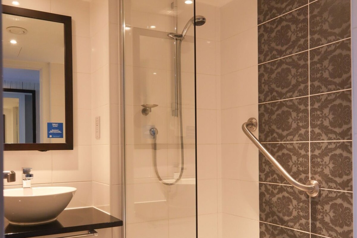 Ein modernes Badezimmer mit einer gläsernen Duschkabine, einem Waschtisch und Wandfliesen mit Muster.