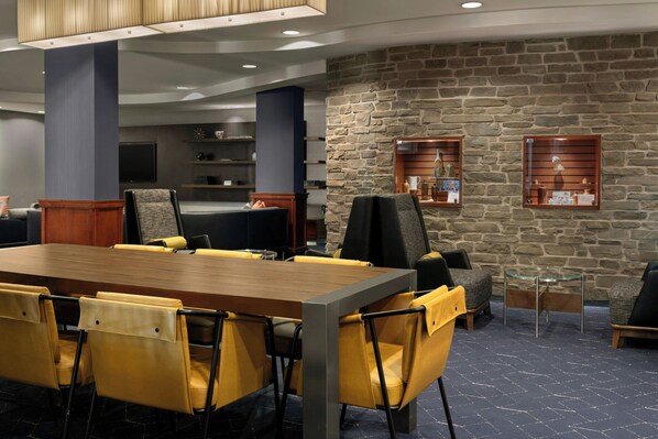 A conference room with a long table, yellow chairs, a stone wall, and built-in shelves with decorative items. - Courtyard by Marriott Halifax Downtown (Halifax)