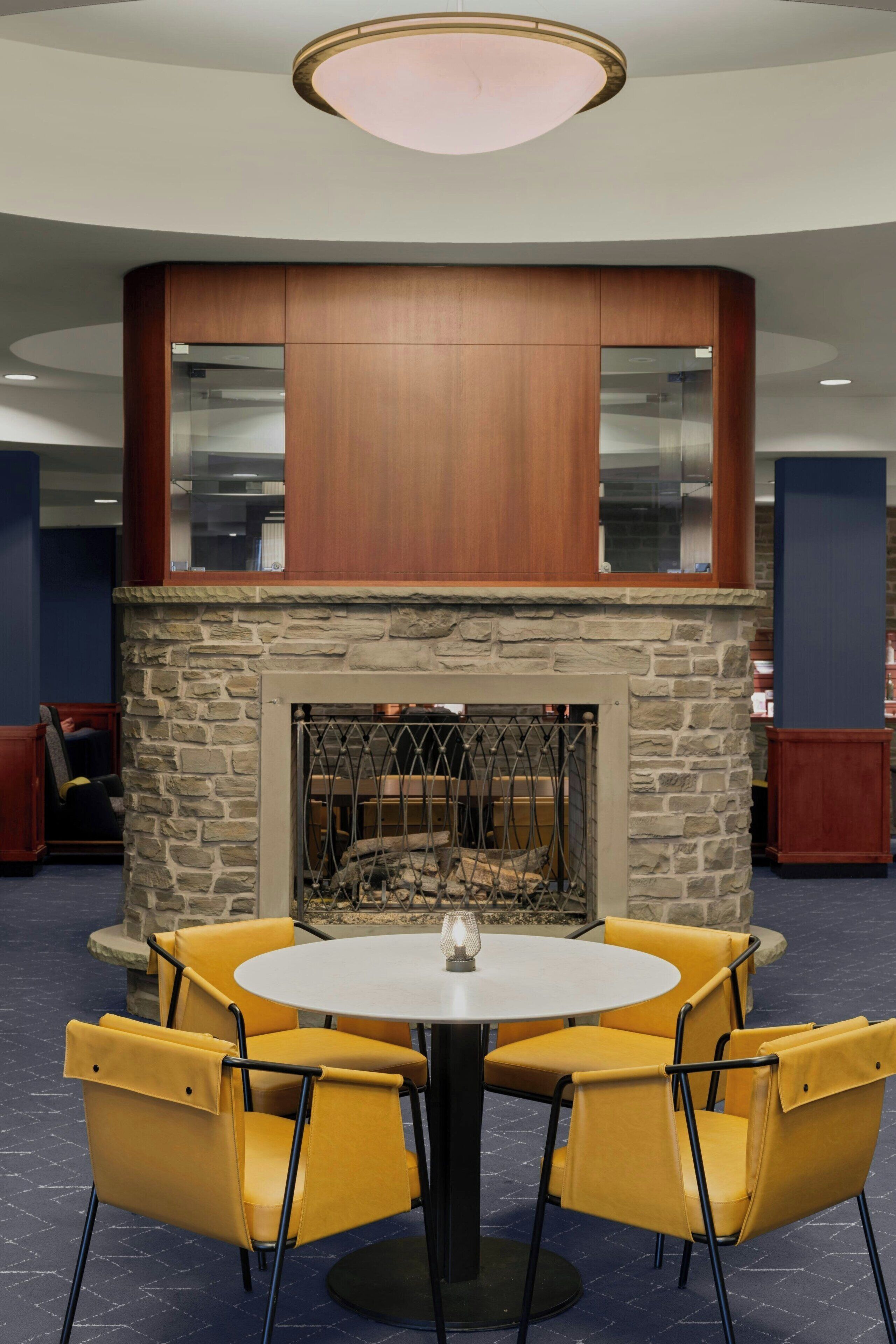 A round table with four yellow chairs, a stone fireplace, and a wooden ceiling structure.