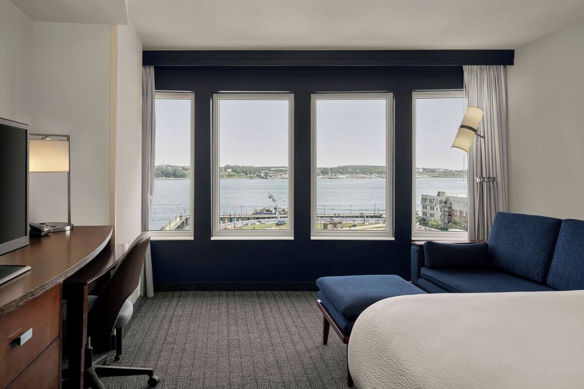 A hotel room with a large window, a bed, a desk, and a chair.