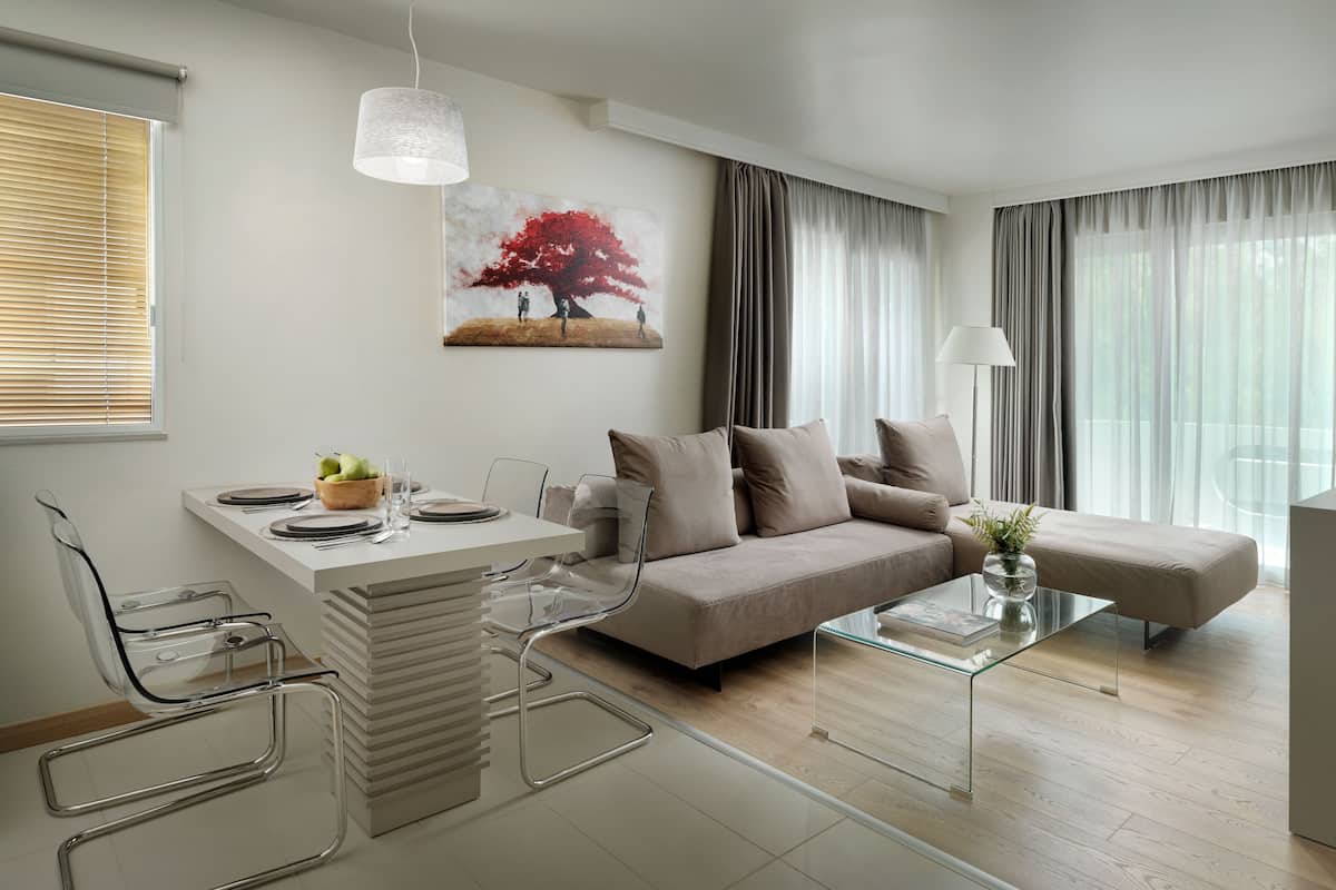 A modern living room with a sofa, a glass coffee table, and a dining area with a white table and clear chairs.