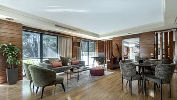 A modern living room with a sofa, coffee table, and chairs, large windows with curtains, and a dining area with a table and chairs.