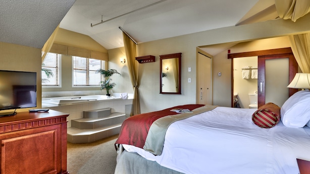 A hotel room with a bed, a TV, a bathroom, and a staircase.
